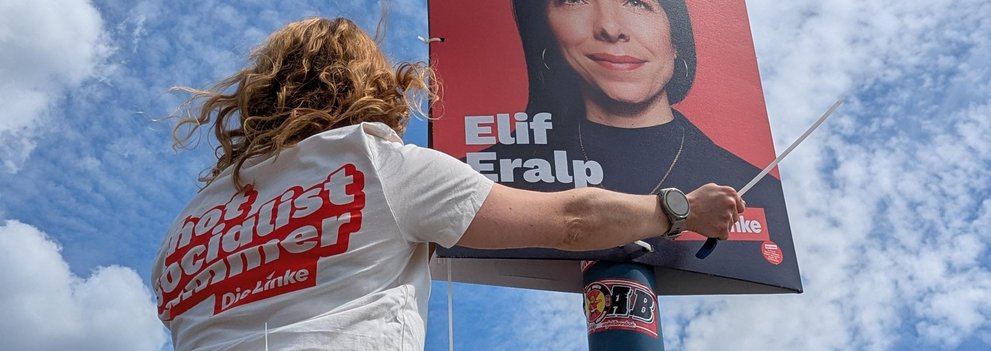 Person hängt Plakat von Elif Eralp (Bürgermeisterkandidatin der Linken) auf